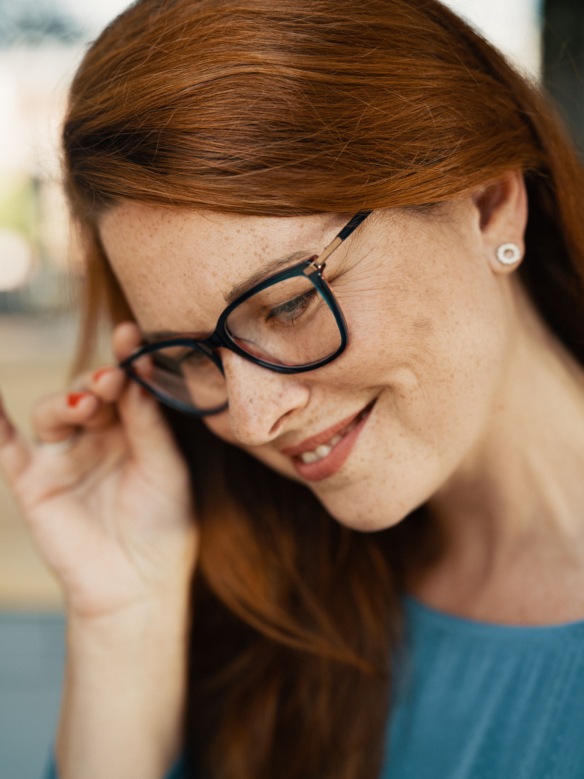 Paní se zrzavými vlasy a výraznými dioptrickými brýlemi. 